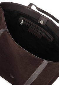 Sac fourre-tout en daim marron avec des accents en cuir, comprenant un intérieur spacieux, une poche zippée et une fermeture magnétique. Texture douce et bretelles robustes.