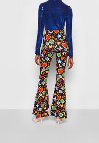 Top de lentejuelas azules de manga larga combinado con pantalones acampanados de estampado floral colorido y corazones sobre un fondo liso. Zapatos de tacón rosas visibles.