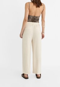 Lightweight, cream linen trousers with a relaxed, wide-leg fit and elastic waistband, paired with a leopard print top. Simple sandals.