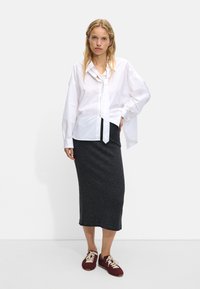 Biała koszula zapinana na guziki z detalem w postaci krawata, połączona z dopasowaną ciemnoszarym spódnicą midi i bordowymi trampkami. Gładkie faktury w kontrastujących kolorach.