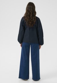 Chemise oversize bleu marine avec des manches volumineuses, associée à un pantalon en denim bleu clair à jambes larges, présentant une finition texturée.