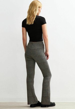 T-shirt noir ajusté à manches courtes associé à un pantalon carotté taille haute à motifs gris et noir. Chaussures noires visibles.