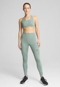 Ljusgrön sport-bh och högmidjade leggings gjorda av ett slätt, stretchigt material; har varumärkeslogotyp och åtsittande design. Svarta träningsskor.