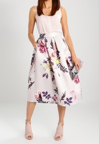 Jupe midi florale en satin rose pâle avec des fleurs violettes et roses éclatantes ; elle présente une taille ajustée et des poches latérales ; associée à un haut clair.