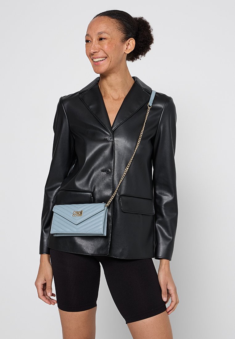 Blazer de cuero negro con solapas afiladas, llevado sobre una blusa negra ajustada y pantalones cortos de motociclista. Bolso cruzado acolchado azul claro con herrajes dorados.