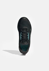 Scarpa sportiva nera con tomaia in mesh testurizzato, dettagli turchesi e lacci neri. Punta arrotondata e suola imbottita per il supporto.