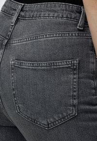 Gros plan d'une personne portant un jean denim gris foncé ajusté, montrant la couture de la poche arrière et de la taille.
