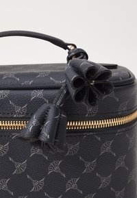 Krožna mornarsko modra usnjena torba z cvetličnim vzorcem, zlatim zadrgo in teksturirano površino. Ima okrasen lok na zadrgi.