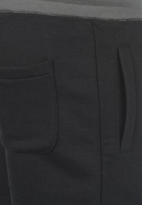 Pantalones de chándal negros con una cinturilla gris, que cuentan con un bolsillo frontal y un bolsillo en la costura lateral. Tejido suave con una textura lisa.