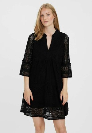 Robe noire en dentelle avec une forme évasée, des manches trois-quarts et un décolleté en V. Présente des motifs complexes au niveau de l'ourlet et des manches.
