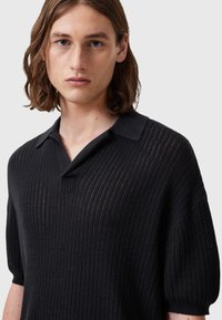 Svart randig pikétröja med kort ärm, med en klassisk krage och en lätt, texturerad stickad design.