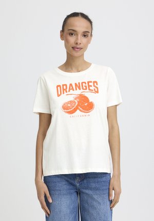 Nő fehér pólóban, amelyen narancssárga szeletelt narancs grafikája és az "ORANGES CALIFORNIA" felirat látható, kék farmerrel, egyszerű háttér előtt.