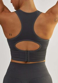 Ciemnoszary sportowy stanik z wycięciem na plecach, prążkowaną fakturą, regulowanymi zapięciami oraz detalem logo na pasku.