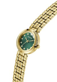 Reloj de pulsera dorado con esfera verde redonda, acentos de rhinestones y una correa metálica texturizada. Presenta manecillas y marcadores de hora minimalistas.