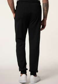 Svarta joggers med elastisk midja, avsmalnande ben och två bakfickor, tillsammans med vita sneakers. Slät tygtextur.