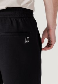 Black joggers with an elastic waistband, featuring a back pocket and a small white embroidered "AX" logo on the right side.