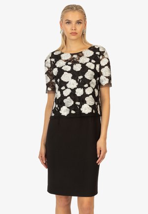 Schwarzes Kleid mit weißem Spitzenblumenüberzug. Kurze Ärmel, taillierte Silhouette, runder Ausschnitt und knielanger Saum. Strukturierte Stoffdetails.