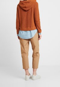 Ruosteenvärinen neulottu huppari hupulla, päällä vaaleansininen farkkupaita. Yhdistetty beigenvärisiin lyhyisiin housuihin ja valkoisiin lenkkareihin.