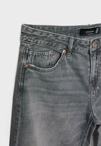 Jean en denim gris délavé montrant la taille avant, les passants de ceinture, le bouton, la fermeture éclair et la petite poche à monnaie avec des rivets métalliques.