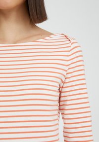 Stribet top med horisontale orange og hvide striber, bred halsudskæring og trekvartærmer med subtil skulderdetalje.