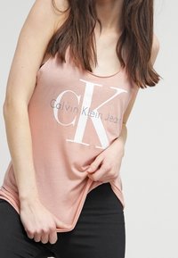 Rosa linne med vitt "Calvin Klein Jeans"-logotyp, med rundad halsringning och avslappnad passform. Tyget verkar mjukt och lätt.