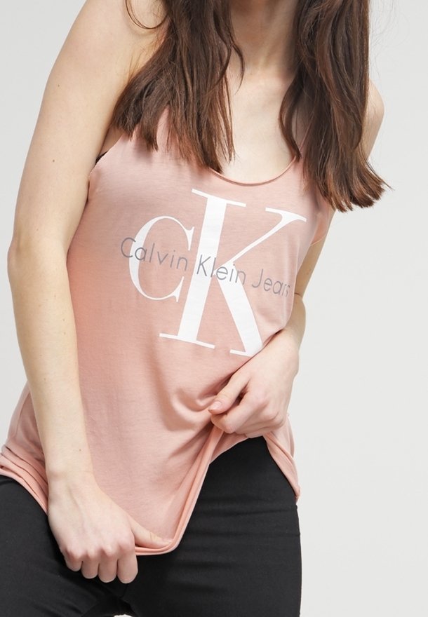 Rosa linne med vitt "Calvin Klein Jeans"-logotyp, med rundad halsringning och avslappnad passform. Tyget verkar mjukt och lätt.