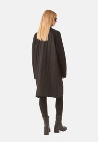 Abrigo negro acolchado con mangas texturizadas, diseño de longitud media y un acabado suave. Combinado con botas de tacón alto negras y leggings.