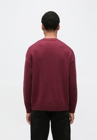 Bordowy sweter z dzianiny z okrągłym dekoltem, ściągaczami na rękawach i dole oraz luźnym krojem. Tekstura tkaniny wydaje się gładka i trwała.