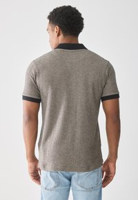 Grå teksturert polo-skjorte med svart krage og ermeakenter, korte ermer og rette kanter. Brukt med lyseblå jeans.