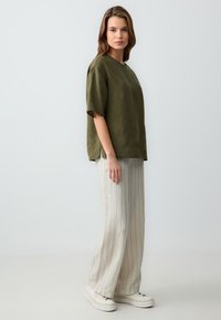 Olijf groene linnen top met korte mouwen en een ronde hals, gecombineerd met lichtgestreepte wijde broek en witte sneakers.