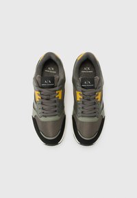 Une paire de baskets Armani Exchange grises et noires avec des accents et des lacets jaunes, vue de dessus sur un fond clair.