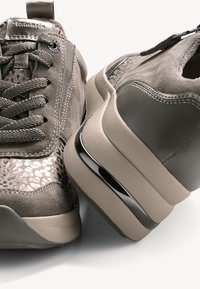 Gros plan de baskets en daim gris avec tissu à motifs, lacets texturés et semelles épaisses beige avec bande d'accent noir.