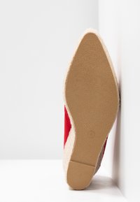 Chaussure rouge à enfiler avec une semelle tissée beige texturée et un bout légèrement pointu. La semelle présente un motif détaillé pour l'adhérence.