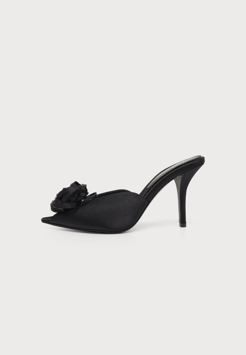 Mule à talon haut en satin noir avec bout pointu ouvert et fleur en tissu décorative à l'avant sur fond blanc.