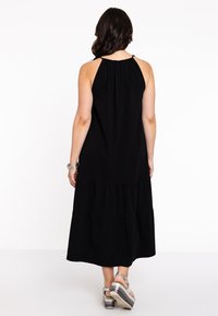 Zwart maxi-jurk met een halternek, elastische gathers, gelaagd design en vloeiende stof. Gemaakt met zilveren platform sandalen.