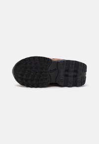 Nike tenisica s potplatima u crnoj gumi s teksturama za grip i kružnim naglascima. Sadrži vidljivo brendiranje i blago podignutu petu.