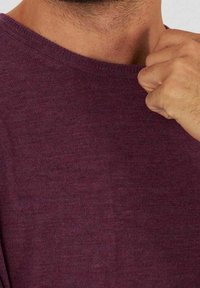 Gros plan sur le cou et la main d'une personne ajustant le col d'un pull en maille bordeaux.