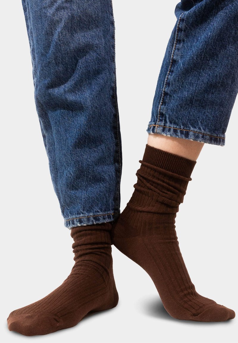 Brązowe skarpetki ze żebrowanym wzorem, w zestawieniu z niebieskimi dżinsami, eksponujące mankiet skarpetki oraz ogólny fason.