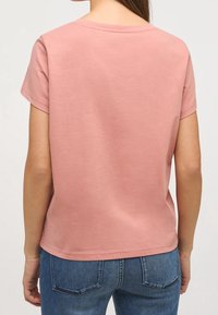 Camiseta de algodón rosa con mangas cortas y cuello redondo, que presenta una textura suave y un ajuste relajado. Detalle de costura visible a lo largo del dobladillo.