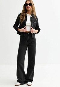 Chaqueta de mezclilla negra y jeans de cintura alta, combinados con una blusa corta blanca y gafas de sol negras. Presenta un diseño de pierna ancha y detalles de botones.