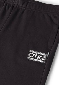 Zwarte joggingbroek gemaakt van zachte stof, met een elastische tailleband en een wit logolabel aan de linkerkant. Eenvoudig ontwerp zonder patronen.