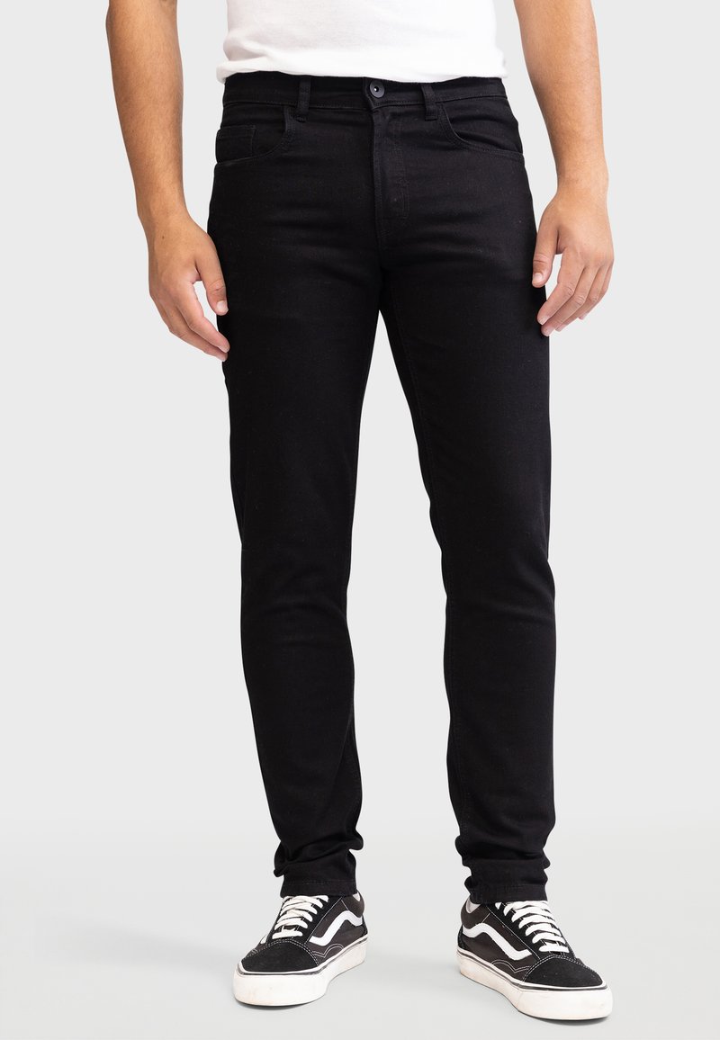Vaqueros de denim negro con un ajuste slim, con cierre de botón, bolsillos frontales y traseros. Llevados con zapatillas negras y blancas.