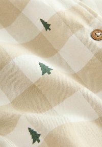 Beige och krämfärgad rutig tyg med små gröna trämotiv, mjuk textur och en accent av en träknapp.