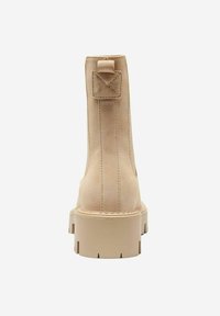 Bottines en suede beige avec une semelle épaisse, dotées d'une languette arrière et de détails de couture subtils. Texture lisse, design minimaliste.