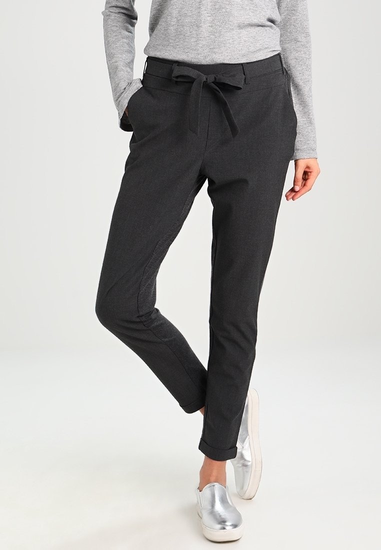 Personne portant un pantalon ajusté gris foncé avec une ceinture nouée à la taille, des ourlets retroussés, un haut à manches longues gris et des chaussures argentées métalliques à enfiler.