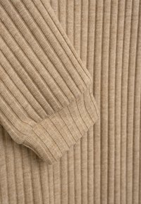 Beige Rippstrickpullovermaterial mit einer strukturierten Oberfläche. Der Ärmel zeigt ein Bündchendesign, das das vertikale Rippmuster hervorhebt.