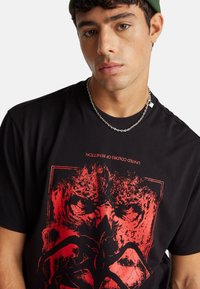 Camiseta negra con un diseño gráfico en rojo intenso que presenta formas abstractas y rostros. Cuello redondo, mangas cortas y material suave.