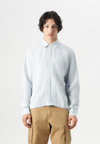 Light blue striped button-up shirt with a collared neck, long sleeves, and a chest pocket, paired with beige cargo pants.