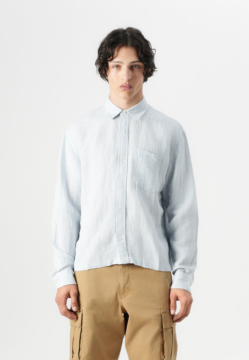 Camisa de botones a rayas azul claro con cuello, mangas largas y un bolsillo en el pecho, combinada con pantalones cargo beige.