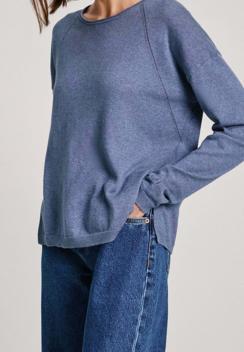 Pull en maille bleu avec manches raglan, encolure ronde, poignets et ourlet côtelés, associé à un jean en denim bleu taille haute.